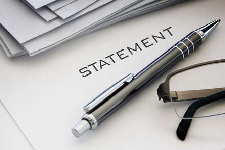 Papier sur lequel la déclaration est écrite. À côté, un stylo à bille noir et des lunettes.