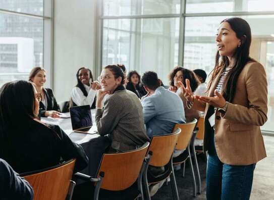Frau steht vor größerer Gruppe mit Männern und Frauen und erklärt Frau steht vor größerer Gruppe mit Männern und Frauen und erklärt