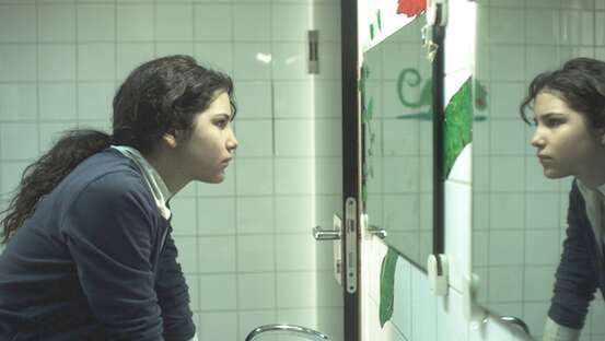 Filmszene. Eine junge Frau schaut sich im Spiegel an.