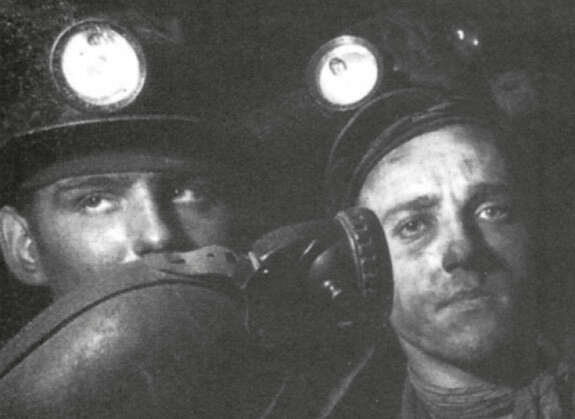 Foto: Schwarweiß, zwei Bergarbeiter mit Helmen auf dem Kopf, Stirnlampen und rußigem Gesicht umgeben von Dunkelheit