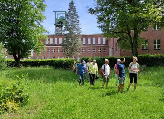 Eine Gruppe von Menschen, die über eine Wiese wandern, im Hintergrund ein Gebäude.