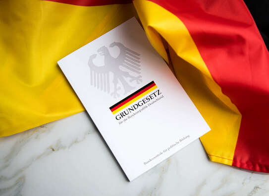 Abbildung der Titelseite einer Broschüre "Grundgesetz" vor der Deutschland-Fahne