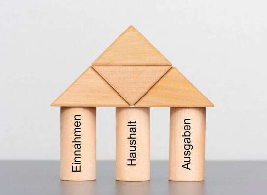 Holzwürfel als Haus aufgebaut mit den Schriftzügen Haushalt, Einnahmen, Ausgaben