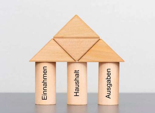 Holzwürfel als Haus aufgebaut mit den Schriftzügen Haushalt, Einnahmen, Ausgaben