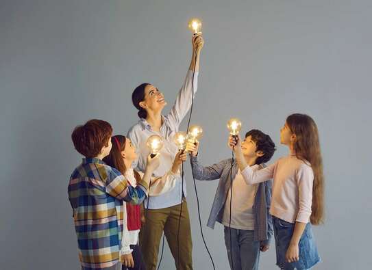 Eine junge Frau und vier Kinder halten jeweils eine leuchtende Glühbirne hoch