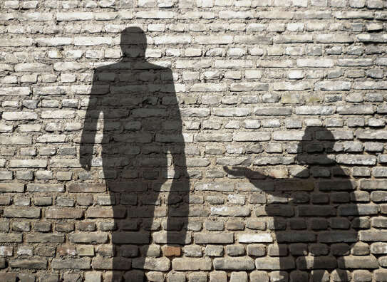 Schatten eines Mannes mit Aktenkoffer, der an einer sitzenden Person mit ausgestreckter Hand vorbeigeht