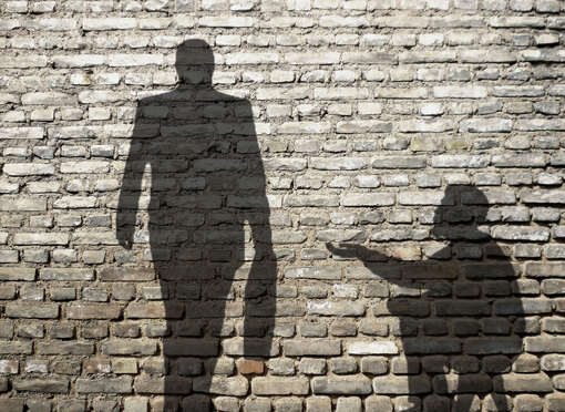 Schatten eines Mannes mit Aktenkoffer, der an einer sitzenden Person mit ausgestreckter Hand vorbeigeht