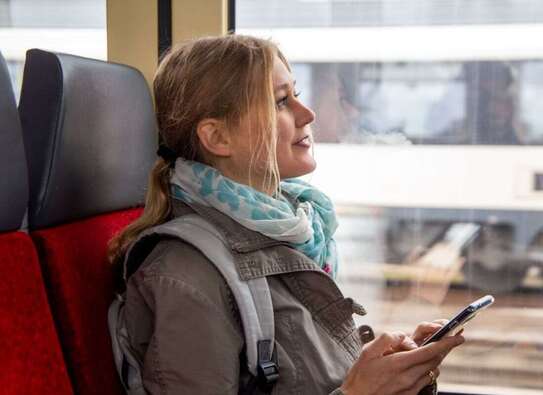 Frau sitzt im Zug und hat Handy in der Hand