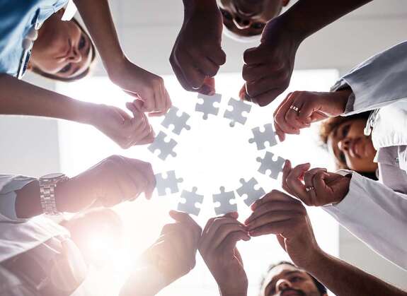 Pflegekräfte stehen im Kreis und halten jeweils ein Puzzle-Teil in die Mitte