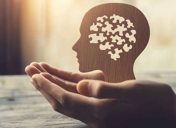 Hand hält eine Siluette von einem Kopf mit vielen Puzzleteilen