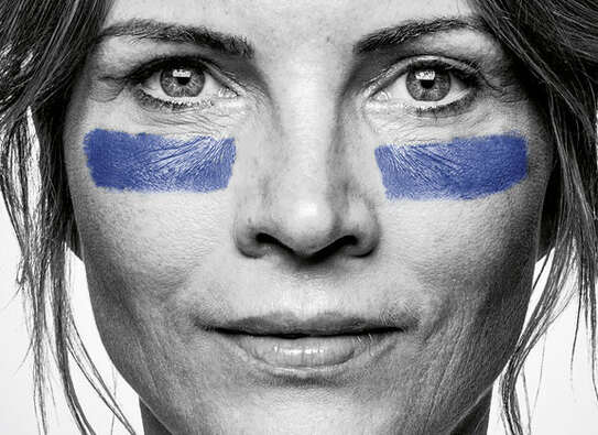 Foto: Schwarzweiß-Bild einer Frau, frontal in die Kamera blickend, sie hat unter ihren Augen jeweils einen blauen Streifen ins Gesicht gemalt