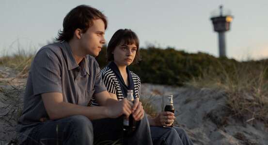 Filmszene. Junger Mann und junge Frau sitzen am Strand in den Dünen.