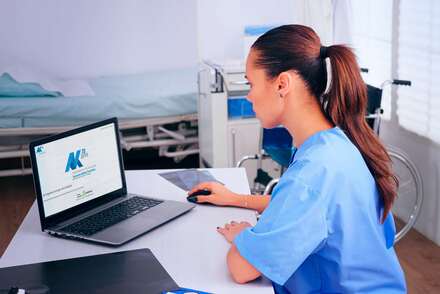 Eine Krankenschwester im blauen Kittel sitzt am Laptop und schaut auf den Bildschirm