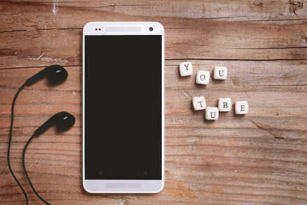 Smartphone and headphones on wooden background. Youtube letter written with wooden cubes