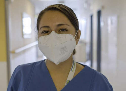 Foto: Eine junge, mexikanische Pflegekraft in Arbeitskleidung und mit Mundschutz, im Hintergrund der Flur eines Krankenhauses