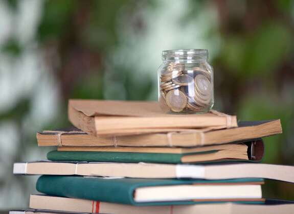 Glas mit Geldmünzen, dass auf einem Stapel Lehrbücher steht