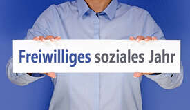 Person, deren Gesicht nicht sichtbar ist und die ein Schild mit der Aufschrift "Freiwilliges Soziales Jahr" in die Kamera hält