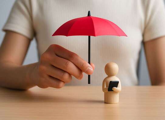 Frau hält roten Schirm über eine Holzfigur mit Notebook im Arm